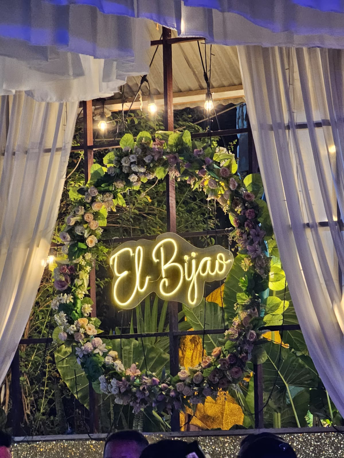 Entrada decorada del salón El Bijao con letrero iluminado, flores tropicales y cortinas elegantes